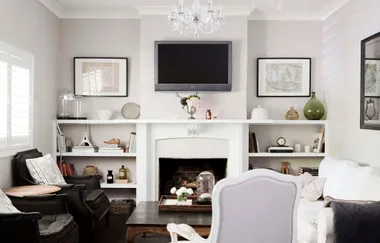 Living room with gray walls, TV above fireplace, white shelves, and black armchairs.