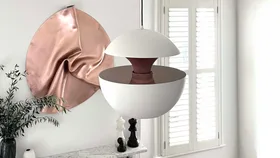 White modern pendant light, copper wall art, chess pieces, plant, and white shutters in a minimalist room.