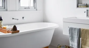 A clean, modern bathroom with a white freestanding bathtub, towels, and bath accessories on a wooden rack.