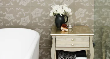 Elegant bathroom with floral wallpaper, a vase of flowers on a wooden table, and a white bathtub.