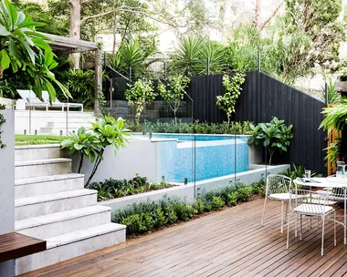 Backyard with pool next to a deck with a dining table and chairs.
