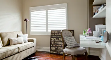 Cozy home office with beige sofa, decorative pillows, wall art, and a desk with flowers and books.