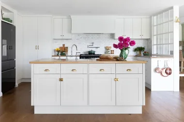 Bright kitchen with white cabinets, a wooden island, pink flowers in a vase, and stainless steel fixtures.