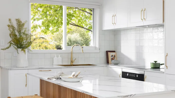 A white kitchen with timber details, including a ribbed island profile and woven bar stools.