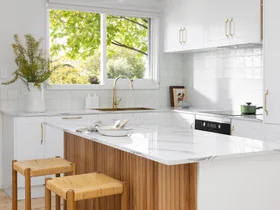 A white kitchen with timber details, including a ribbed island profile and woven bar stools.