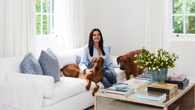 Krissy Marsh and her dog sitting on a sofa in the all-white living room.