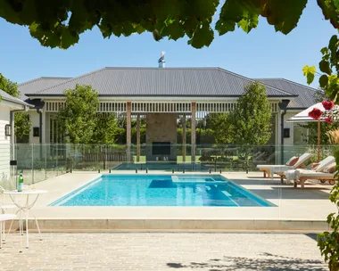 An outdoor pool area with white loungers leading to an alfresco area.