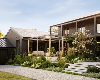 A modernist timber and steel two-storey home with sprawling white and green plant beds.