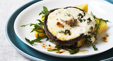 Stuffed portobello mushroom with creamy topping, garnished with arugula and sauce, served on a white plate.