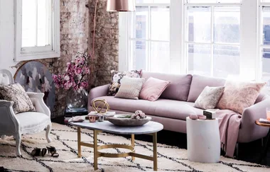 Living room with a pink sofa, patterned cushions, metallic coffee table, and brick accent wall with pink flowers.