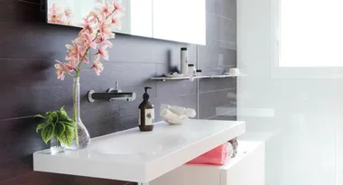 Modern bathroom with white sink, pink orchids, soap dispenser, and neatly folded towels under a bright window.
