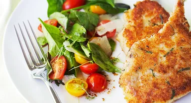 Crispy breaded chicken on a plate with a fresh salad of mixed greens and cherry tomatoes, served with a fork.
