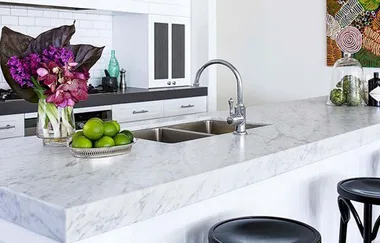 Sleek kitchen with marble countertop, flowers, limes, and a modern faucet, against a backdrop of white cabinets and decor.