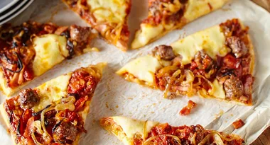 Sliced pizza topped with sausage, onions, and cheese on parchment paper.