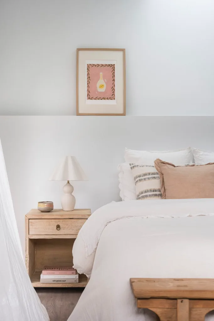 A mediterranean coastal style bedroom with white bed linen, a timber bedside table and a white bedside table lamp.