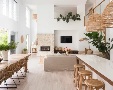 An open plan kitchen, dining and living area with mediterranean coastal style interiors, including white, reclaimed timber and a stone wall.