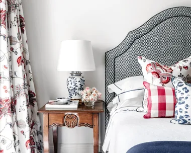 A guest bedroom with floral curtains, a timber side table and grey lined bedhead.