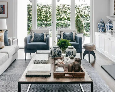 A formal style living area with blue armchairs, bifold glass doors and a timber coffee table.