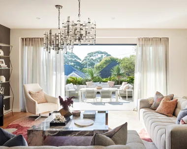 An open plan living room with a grey couch, marble coffee table and one wall painted white and one wall painted black. The sliding door opens to an outdoor living area.