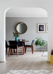 Dining area with round table, blue chairs, potted plants, round mirror on gray wall, and wooden floor.