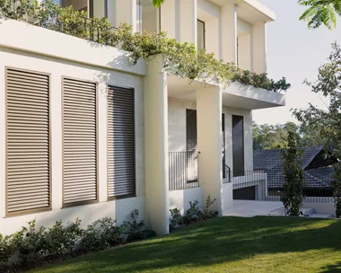 Modern two-story house with large windows, surrounded by greenery and trees, under a clear blue sky.