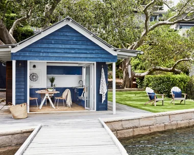 The blue cladded boatshed and two deck chairs on a lawn facing the bay.
