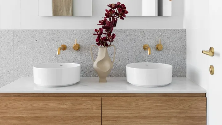 A white and grey ensuite with a timber vanity, gold tapware and arched mirrors.