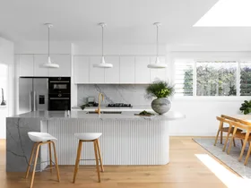 A white coastal-style kitchen with a fluted island and grey marble.