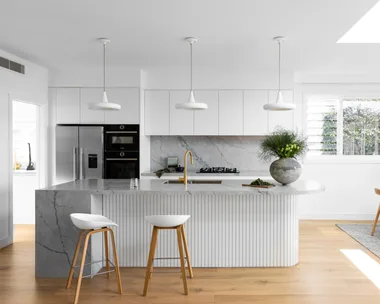 A white coastal-style kitchen with a fluted island and grey marble.