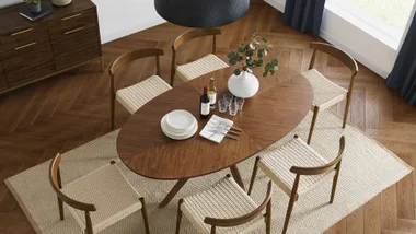 Dining table set with six chairs, plates, wine bottles, glasses, and a vase on a wooden floor with a rug.