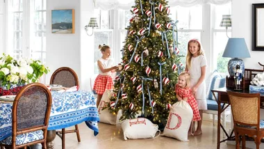 Girls decorating a Christmas tree with ribbons and ornaments in a festive room with a blue and white table setting.