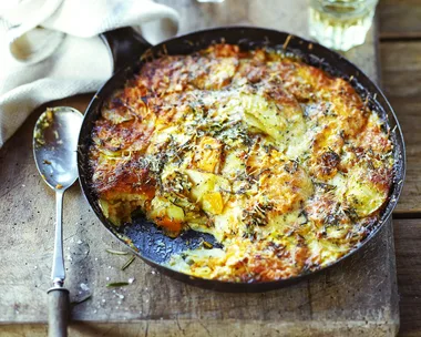 Potato, squash and pumpkin gratin in cast iron pan on serving board with white wine
