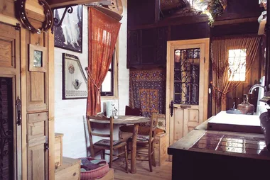 Rustic kitchen with wooden furniture, colorful tapestry, round table, and art on walls, exuding a cozy, vintage vibe.