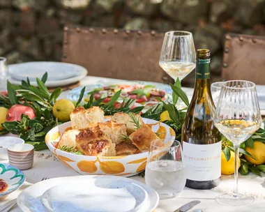 An outdoor tablescape with wine and a bowl of focaccia bread.