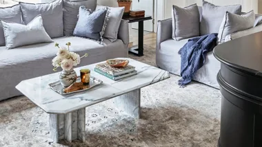 Cozy living room with gray sofas, marble coffee table, flower vase, and books, on a patterned rug.