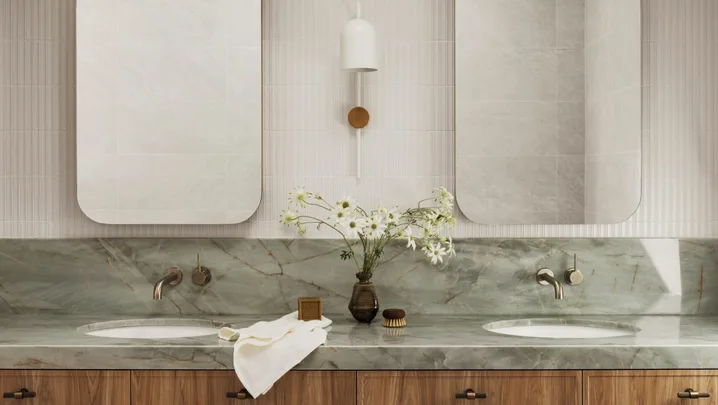 A bathroom vanity with timber cupboards, sage green stone benchtop and splashback, two rectangular mirrors and white wall tiles. A skylight is above.
