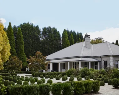 A country house surrounded by rounded topiary plants.