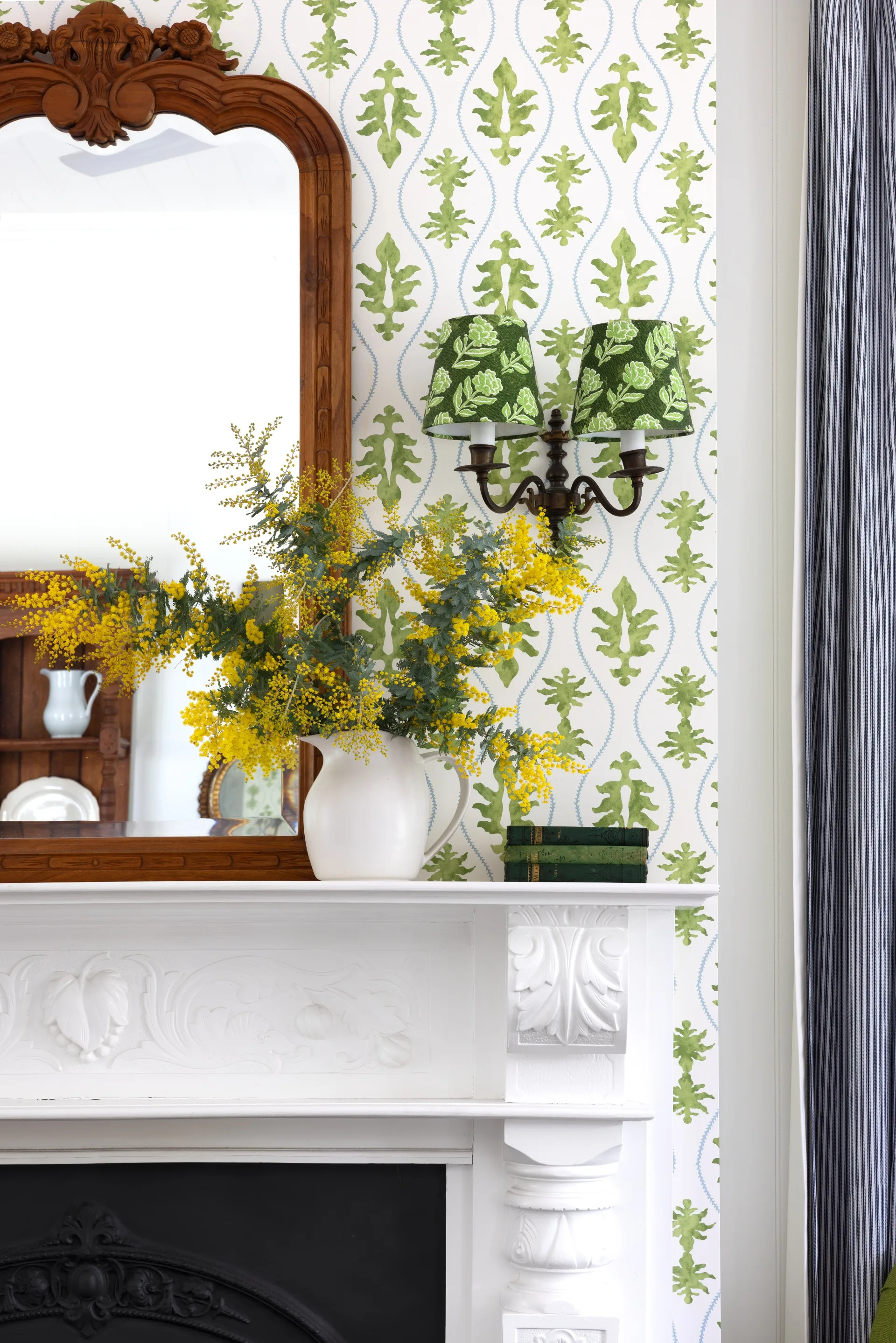 A white antique fireplace in the living area surrounded by green patterned wallpaper.