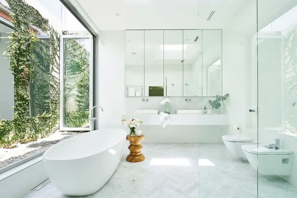 Bright, modern bathroom with a free-standing tub, large mirrors, and a window view of greenery.