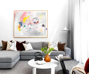 Contemporary living room with a gray sectional sofa, colorful abstract painting, and modern decor on a marble coffee table.