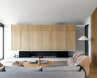 A Scandinavian style living room with fluted timber walls, a fireplace and curved chairs.