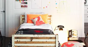 Cozy bedroom with a rustic wooden bed, colorful pillows, a black rotary phone on a nightstand, and wall decorations.