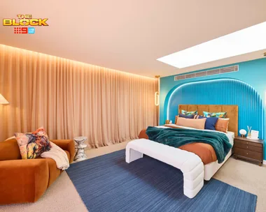 A modern bedroom from "The Block" with a teal accent wall, velvet sofa, and ample lighting.