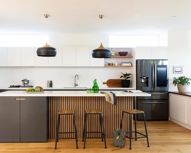 Modern kitchen with black pendant lights, wooden island, bar stools, marble countertop, and stainless steel appliances.